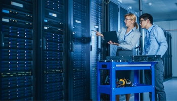 In Technology Research Facility: Chief Engineer Stands in the Middle of the Lab and Uses Tablet Computer. Team of Industrial Engineers, Developers Work on Engine Design Use Digital Whiteboard and Computers